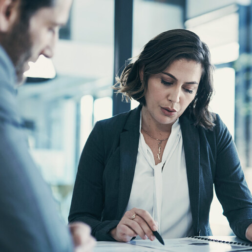 A professional woman in business attire reviews a document with a colleague in a modern office setting. She appears focused, analyzing the details while engaged in discussion.