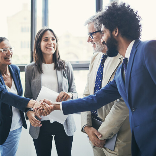 Business professionals in a modern office shaking hands and smiling, representing teamwork, partnership, and corporate collaboration.