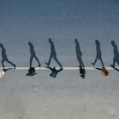 Group of people walking in unison casting long shadows on the pavement, symbolizing teamwork, collaboration, and unity in leadership and business.