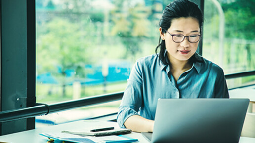Professional woman wearing glasses working on a laptop in a bright, modern workspace, representing productivity, remote work, and business strategy.