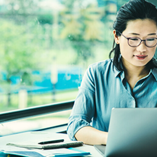 Professional woman wearing glasses working on a laptop in a bright, modern workspace, representing productivity, remote work, and business strategy.