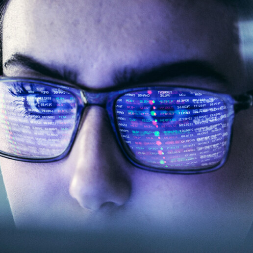 Close-up of a woman wearing glasses with lines of code reflected on the lenses, indicating deep focus on data analysis or programming in a high-tech environment.