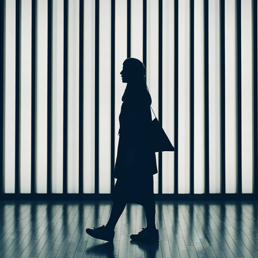 Silhouette of a woman walking past an illuminated modern backdrop, symbolizing progress, innovation, and forward-thinking leadership.