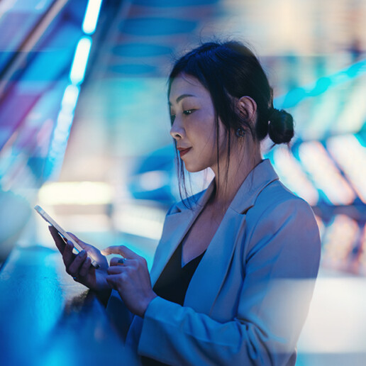Young woman in a modern, futuristic setting illuminated by vibrant blue and pink neon lights, engaging with her smartphone while leaning on a railing.