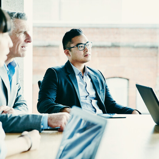 Diverse group of business professionals in a modern conference room, engaged in a strategic discussion with laptops open, representing leadership and workforce planning.