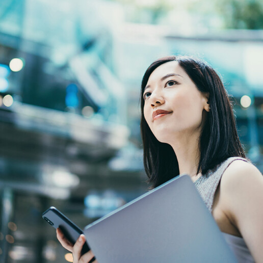 Confident professional woman holding a laptop and smartphone in a modern glass building, symbolizing business leadership, technology, and innovation.