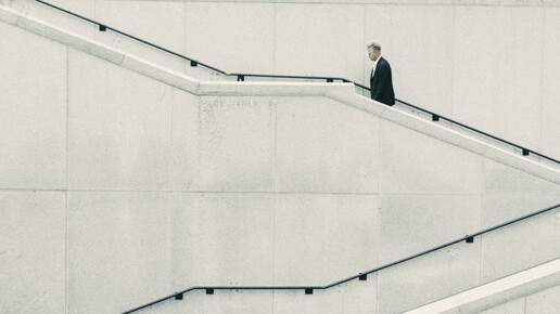 Person in business attire walking alone up a modern concrete staircase against a minimalist wall.