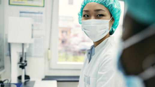 Healthcare professional wearing a surgical mask and green cap in a medical setting, representing frontline workers, patient care, and hospital workforce resilience.