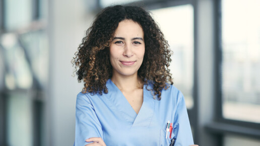 Confident female healthcare professional in blue scrubs, standing in a bright medical facility with arms crossed, representing workforce retention and job satisfaction in healthcare.