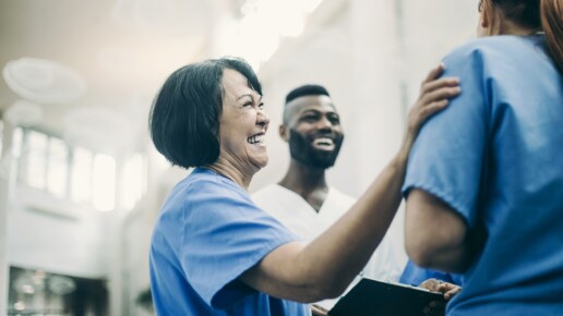 Healthcare workers in scrubs smiling and talking in a hospital corridor.