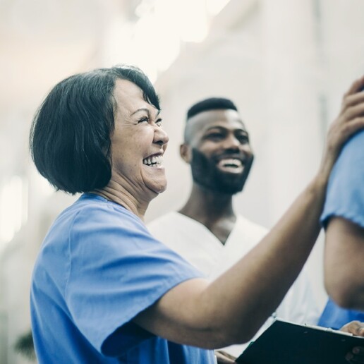 Healthcare workers in scrubs smiling and talking in a hospital corridor.